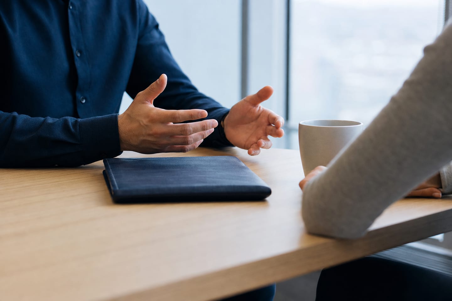 A conversation across a bright table, one person explaining while the other listens, faces out of frame