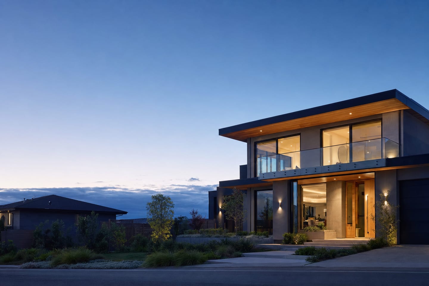 A contemporary two-story home with large windows glowing at dusk, seen from the street